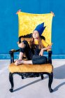 Thoughtful teenager in golden paper crown sitting on throne like king on blue background with eyes closed — Stock Photo