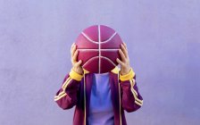 Anonyme Senior-Basketballspielerin in Sportbekleidung, die Gesicht mit Ball auf lila Hintergrund bedeckt — Stockfoto