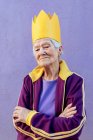 Selbstbewusste ältere Athletin in Sportbekleidung und dekorativer Krone blickt mit verschränkten Armen auf lila Hintergrund in die Kamera — Stockfoto