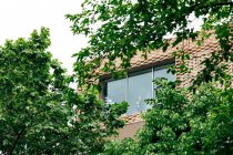 Знизу через вікно вигляд жінки в стильному вбранні, що стоїть в сучасному будинку з геометричними елементами на стінах біля зелених дерев і рослин вдень — стокове фото