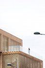 De dessous de femelle en tenue élégante debout sur le balcon du bâtiment moderne avec des éléments géométriques sur les fenêtres tout en utilisant une tablette près de balustrades en verre sous un ciel lumineux — Photo de stock