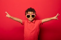 Criança legal vestindo brilhantes óculos de sol Feliz Aniversário mostrando gesto de paz no fundo vermelho em estúdio — Fotografia de Stock