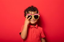 Cooles Kind mit heller Happy Birthday Sonnenbrille auf rotem Hintergrund im Studio — Stockfoto