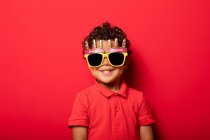 Niño fresco con brillantes gafas de sol Happy Birthday sobre fondo rojo en el estudio - foto de stock