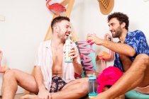 Divertente eccitato diversi fidanzati omosessuali adulti in abiti estivi con bevande fingendo di essere sulla spiaggia con fenicottero rosa e divertirsi insieme — Foto stock