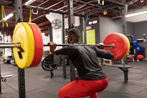 Back view young African American male athlete in activewear and face mask lifting heavy metal barbell while training in gym during coronavirus pandemic — Stock Photo