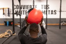 Rückenansicht eines jungen schwarzen Sportlers in aktiver Kleidung beim Bauchmuskeltraining mit Medizinball während des funktionellen Trainings im modernen Fitnessstudio — Stockfoto