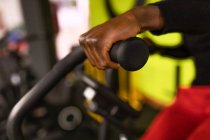 Crop African American male athlete exercising on cycling machine during training in gym against bright yellow background — Stock Photo