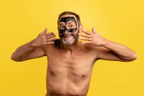 Smiling middle aged male showing black peel off mask on face while looking at camera on yellow background — Stock Photo
