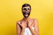 Cheerful middle aged female with black peel off mask standing on yellow studio background looking a camera — Stock Photo