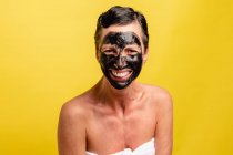 Fröhliche Frau mittleren Alters mit schwarzer abgeblätterter Maske steht auf gelbem Studiohintergrund und schaut in die Kamera — Stockfoto