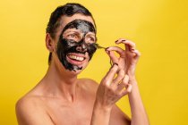 Cheerful middle aged female with black peel off mask standing on yellow studio background looking a camera — Stock Photo