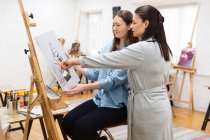 Вид збоку художниці навчає жінку малювати на мольберті під час майстер-класу в творчій студії — стокове фото