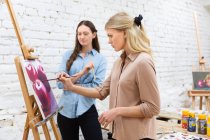 Seitenansicht der Künstlerin, die Frau Malerei Bild auf Staffelei während eines Workshops im kreativen Atelier unterrichtet — Stockfoto