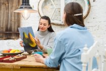 Fröhliche Künstlerinnen trinken Getränke und diskutieren über Malerei am Tisch im Kunstworkshop — Stockfoto