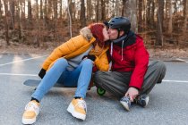 Восхитительная пара, сидящая на скейтборде и скутере во время поцелуев и веселья на парковке осенью — стоковое фото