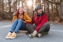 Entzücktes Paar sitzt auf Skateboard und Roller und hat Spaß auf dem Parkplatz im Herbst — Stockfoto