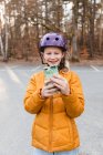 Adolescente joyeuse en casque prenant des photos sur téléphone portable tout en se tenant sur le parking dans le parc d'automne et en regardant la caméra — Photo de stock