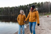 Zufriedene Mutter und Teenager halten Händchen und spazieren am Teich im Wald entlang, während sie das Herbstwochenende genießen — Stockfoto