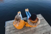 Dall'alto di madre irriconoscibile e ragazza adolescente seduta su banchina di legno vicino allo stagno insieme in autunno — Foto stock