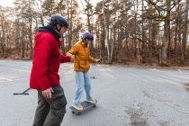 Батько тримає руку підліткової дочки, їде на скейтборді в осінньому парку під час вихідних — стокове фото