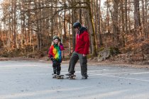 Carefree father and daughter in helmets riding skateboards in park and having fun together during weekend — Stock Photo