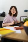 Вид сбоку женщины, рисующей картину на графическом планшете, сидя за столом в домашнем офисе — стоковое фото
