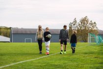Casal alegre e filhos adolescentes em sportswear reunião no campo de futebol verde para jogar futebol juntos no fim de semana — Fotografia de Stock