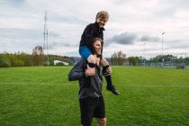 Père joyeux portant adolescent garçon sur l'épaule tout en se tenant sur le terrain de football — Photo de stock