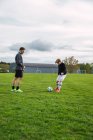 Fröhlicher Vater und Teenager-Sohn in Aktivkleidung spielen Fußball, während sie Ball kicken und über das Feld rennen — Stockfoto