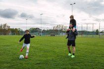 Веселий хлопчик-підліток штовхає м'яч і грає у футбол у полі з батьком і братом у вихідні — стокове фото