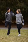 Corpo pieno di vecchia coppia che indossa abbigliamento sportivo riscaldandosi prima dell'allenamento e aiutandosi a vicenda nel parco — Foto stock