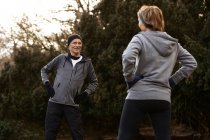 Positives altes Paar in Sportkleidung mit ausgestreckten Armen beim Training im Park und beim Betrachten des anderen — Stockfoto