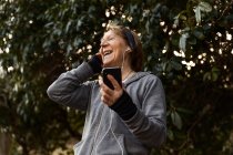 Low angle of old female in sportswear listening to music in earphones during outdoor training — Stock Photo