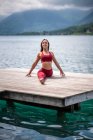 Ruhige Frau sitzt in Hanumanasana auf einem hölzernen Steg, während sie im Sommer Yoga praktiziert und die Beine am See streckt — Stockfoto