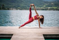 Flexible ruhige Hündin in Utthita Vasishthasana praktiziert Yoga und Stretching Beine auf hölzernen Pier in der Nähe Teich im Sommer — Stockfoto