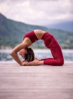 Vista laterale della femmina flessibile che fa yoga a Kapotasana sul molo di legno vicino al lago — Foto stock
