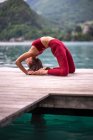 Side view of flexible female doing yoga in Kapotasana on wooden quay near lake — Stock Photo