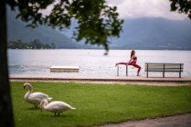 Вид збоку на безтурботну жінку в спортивному одязі, що розтягує ноги і робить розщеплення, практикуючи йогу на дерев'яній набережній біля озера — стокове фото