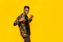 Улыбающийся афроамериканец в модном наряде показывает жест шака на жёлтом фоне в студии — стоковое фото