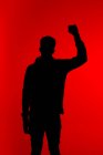 Silhouette of unrecognizable African American male protester standing with clenched fist on red background in studio — Stock Photo
