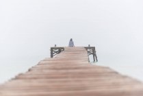 Повернення до нерозпізнаної жінки, яка сидить на дерев'яному пірсі біля моря в туманний ранок влітку на Плей - де - Муро в Іспанії. — стокове фото