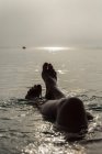 Colheita pernas descalças de fêmea irreconhecível deitada na água do mar e desfrutando de manhã ensolarada durante as férias na Playa de Muro — Fotografia de Stock