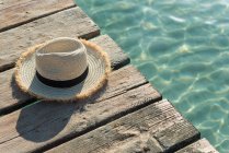 Alto ángulo de sombrero de paja colocado en muelle de madera cerca del mar azul en el día soleado en verano en Playa de Muro - foto de stock