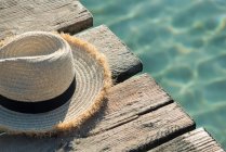 Chapeau de soleil haut angle de paille placé sur un quai en bois près de la mer bleue par une journée ensoleillée en été sur Playa de Muro — Photo de stock