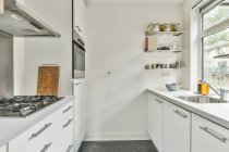 Креативний дизайн кухні з шафами і плитою проти раковини і полиць з баночками в будинку вдень — стокове фото