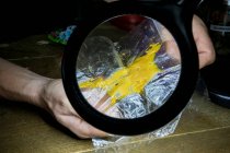 Анонімний чоловік, що демонструє клей марихуани на пластиковому шматочку через збільшувальну лампу в кімнаті — стокове фото
