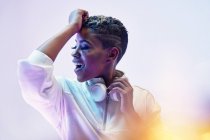 Енергетична етнічна жінка в бездротових навушниках навколо шиї і модний одяг танцює хіп-хоп з відкритим ротом і закритими очима — стокове фото