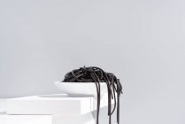 Monolocale minimalista con spaghetti neri di calamaro che cadono dalla ciotola di ceramica piena sul tavolo bianco — Foto stock