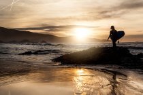 Side view of unrecognizable young woman standing in the shore with surfboard before getting into the sea during sunset on the beach in Asturias, Spain — Stock Photo